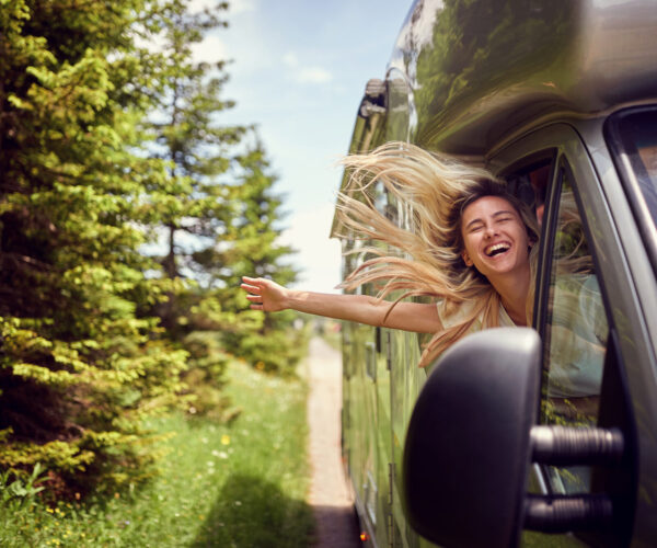 Blonde woman on the window of an rv with hands out smiling enjoy Blonde woman on the window of an rv with hands out smiling enjoying ride.Transport, roadtrip, nature concept.
