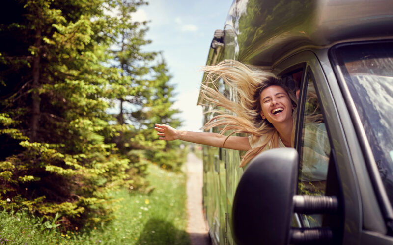 Blonde woman on the window of an rv with hands out smiling enjoy Blonde woman on the window of an rv with hands out smiling enjoying ride.Transport, roadtrip, nature concept.