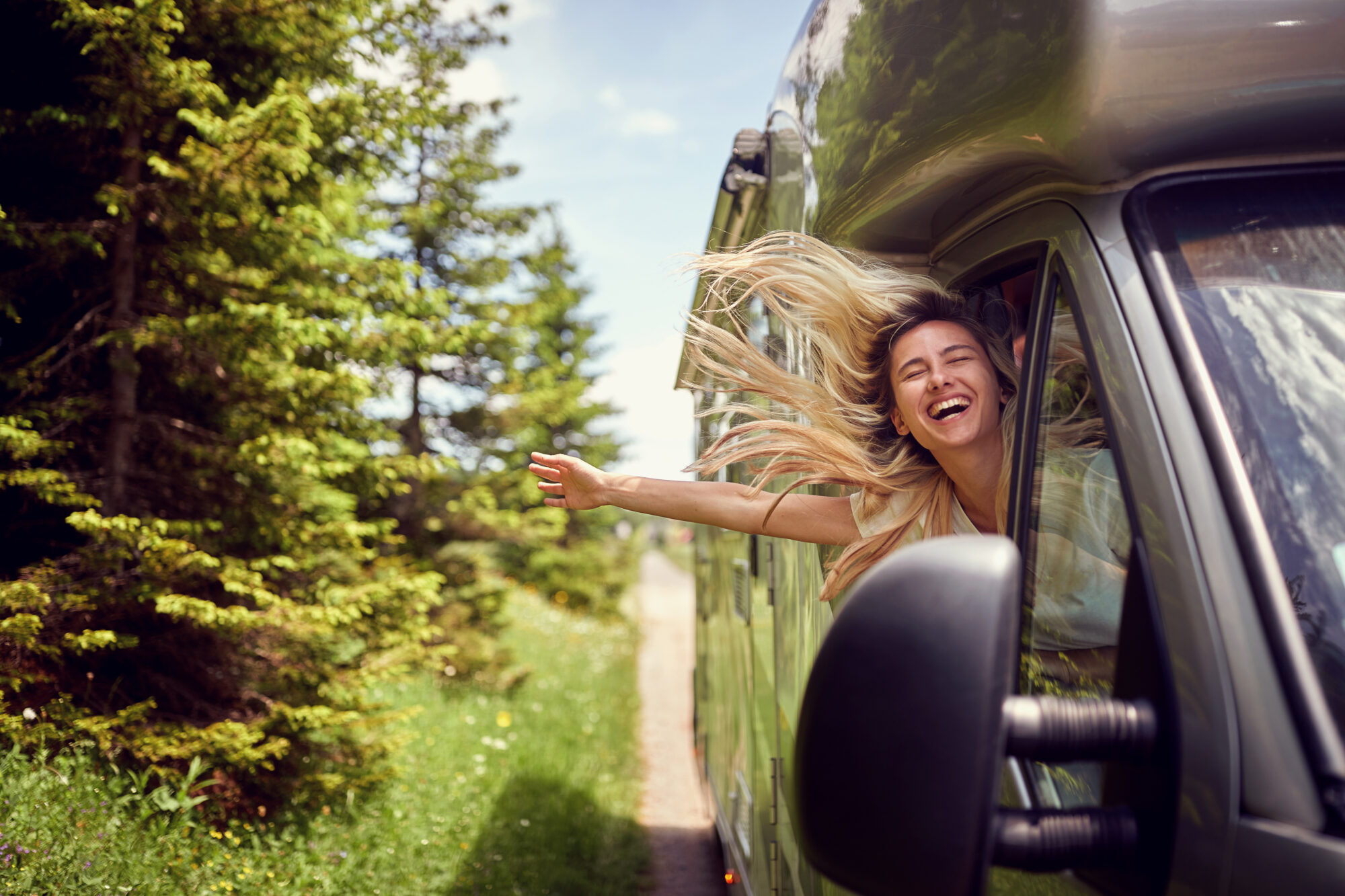 Blonde woman on the window of an rv with hands out smiling enjoy