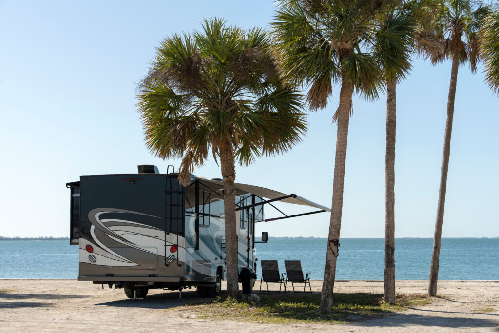 Class A motorhome with awning extended parked under palm trees at a sunny waterfront campsite during winter RV campingClass A motorhome with awning extended parked under palm trees at a sunny waterfront campsite during winter RV camping