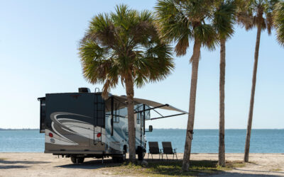 Class A motorhome with awning extended parked under palm trees at a sunny waterfront campsite during winter RV campingClass A motorhome with awning extended parked under palm trees at a sunny waterfront campsite during winter RV camping